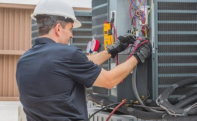 HVAC technician testing electrical components on an outdoor air conditioning unit