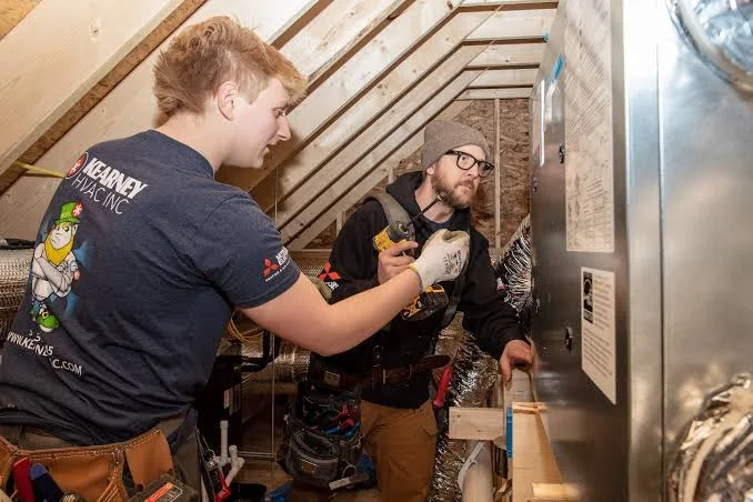 HVAC technicians inspecting an indoor air handler and duct connection